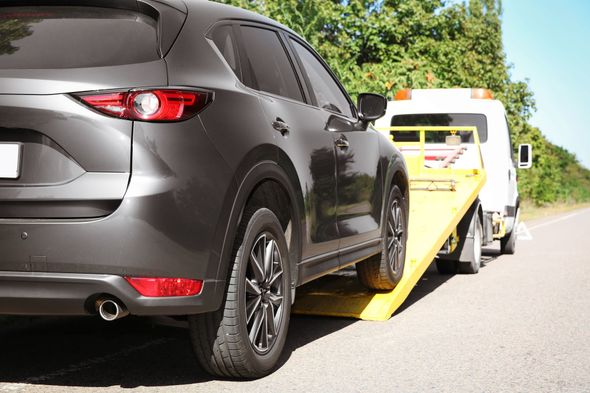 Gray SUV being towed by a tow truck on a road; sunny day.