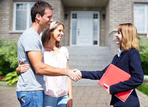 Two people shaking hands with a real estate agent holding a red folder outside a house