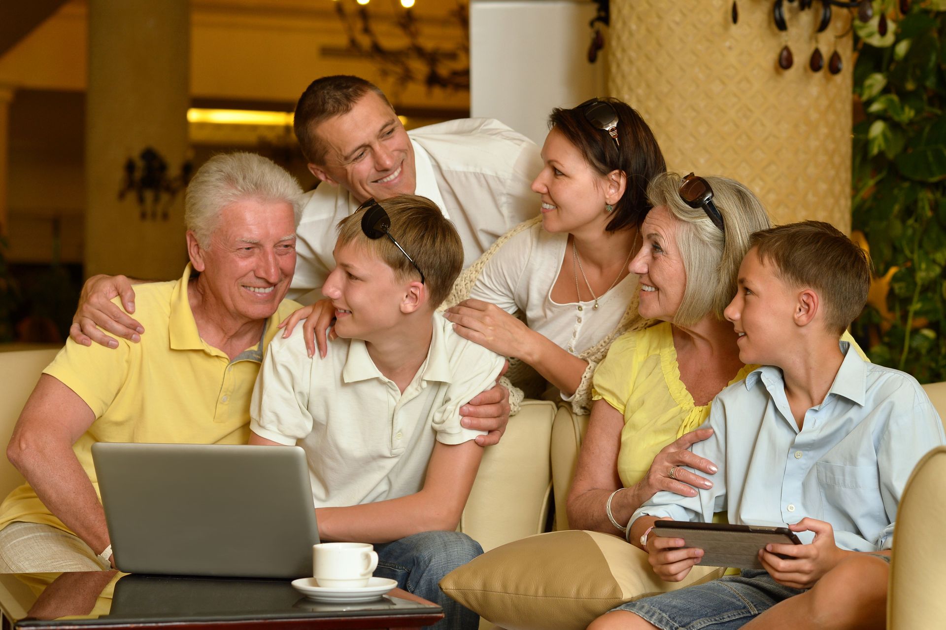 Family gathered on a couch, smiling and chatting around a laptop in a warm living room.
