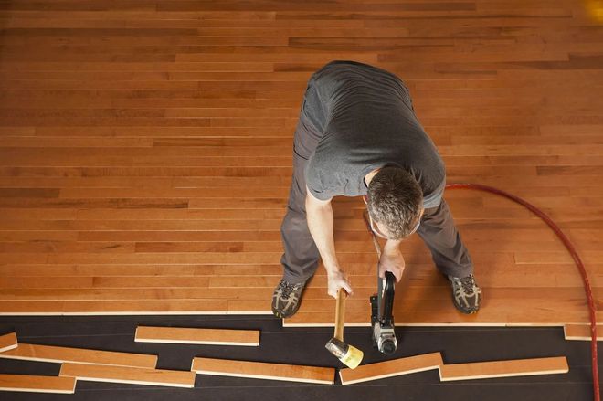 Man installing hardwood floor planks with a hammer and nail gun.