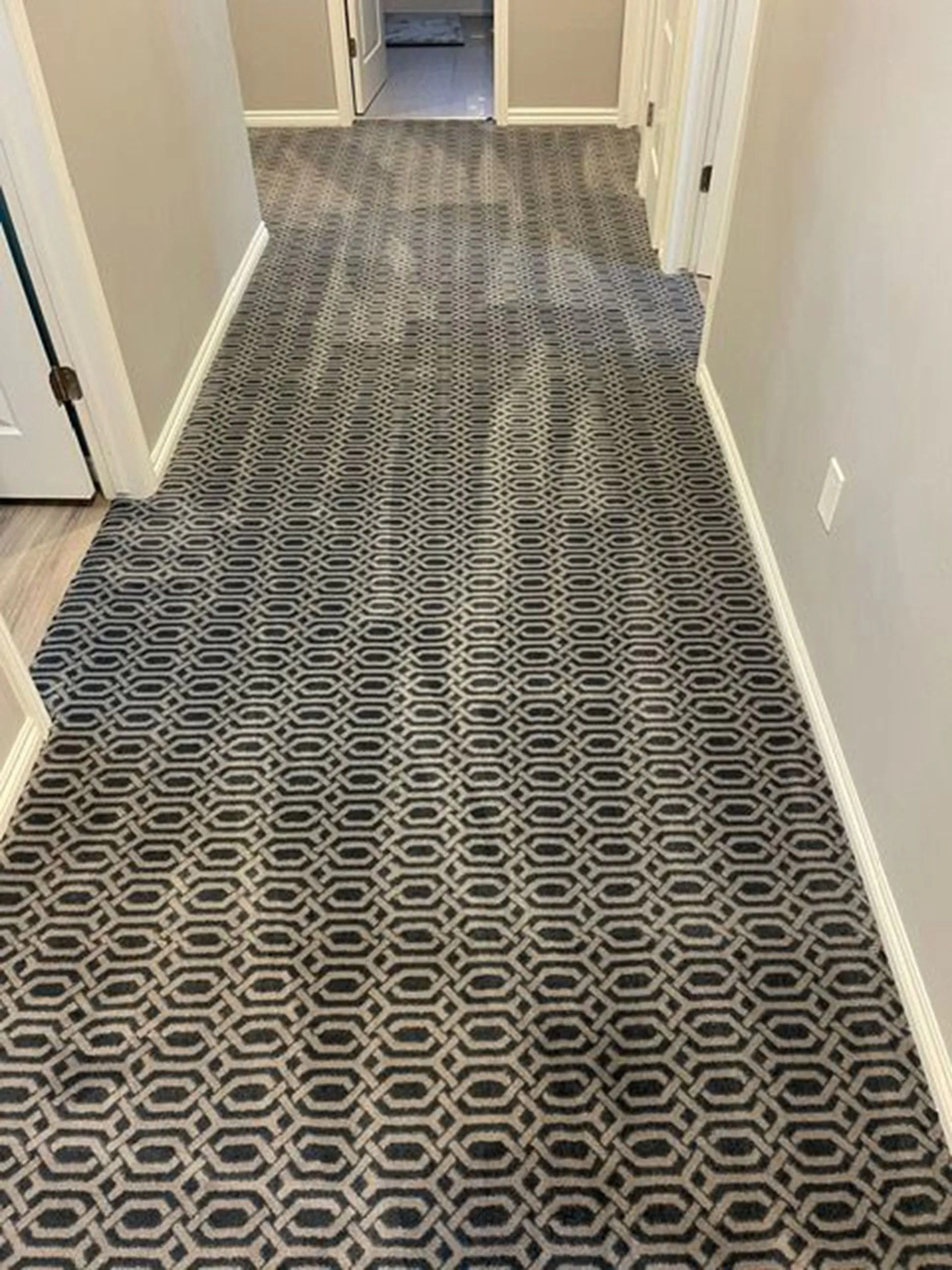 Hallway with patterned gray and black carpet, framed by beige walls and white trim.