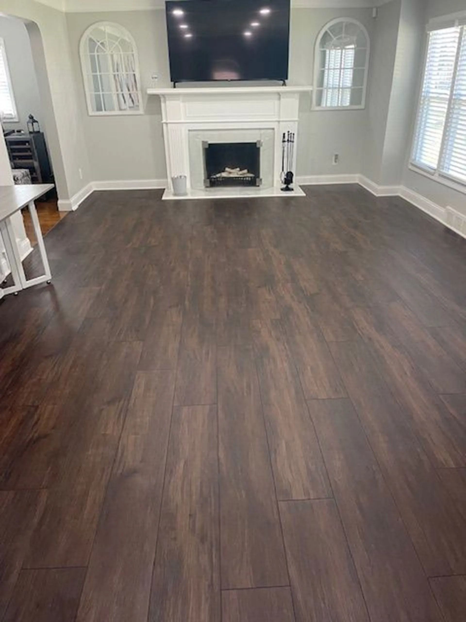Dark wood floor in a living room with a fireplace, TV, and window with blinds.