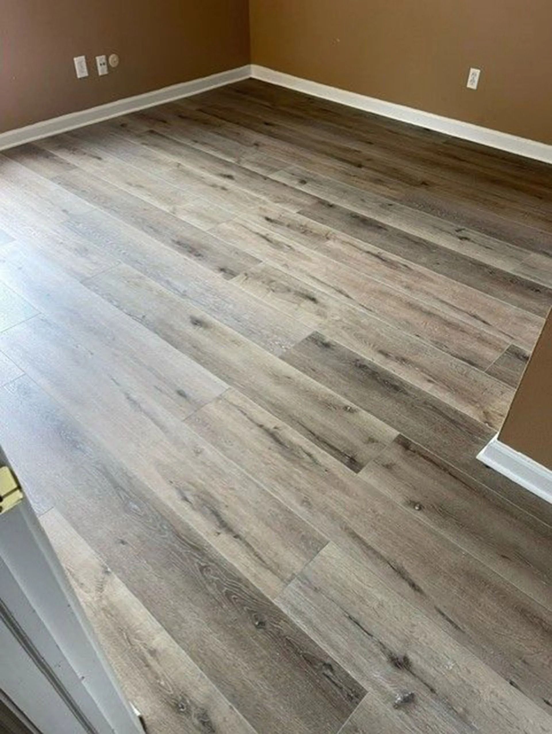 Wooden-look flooring in a room with white baseboards and tan walls.