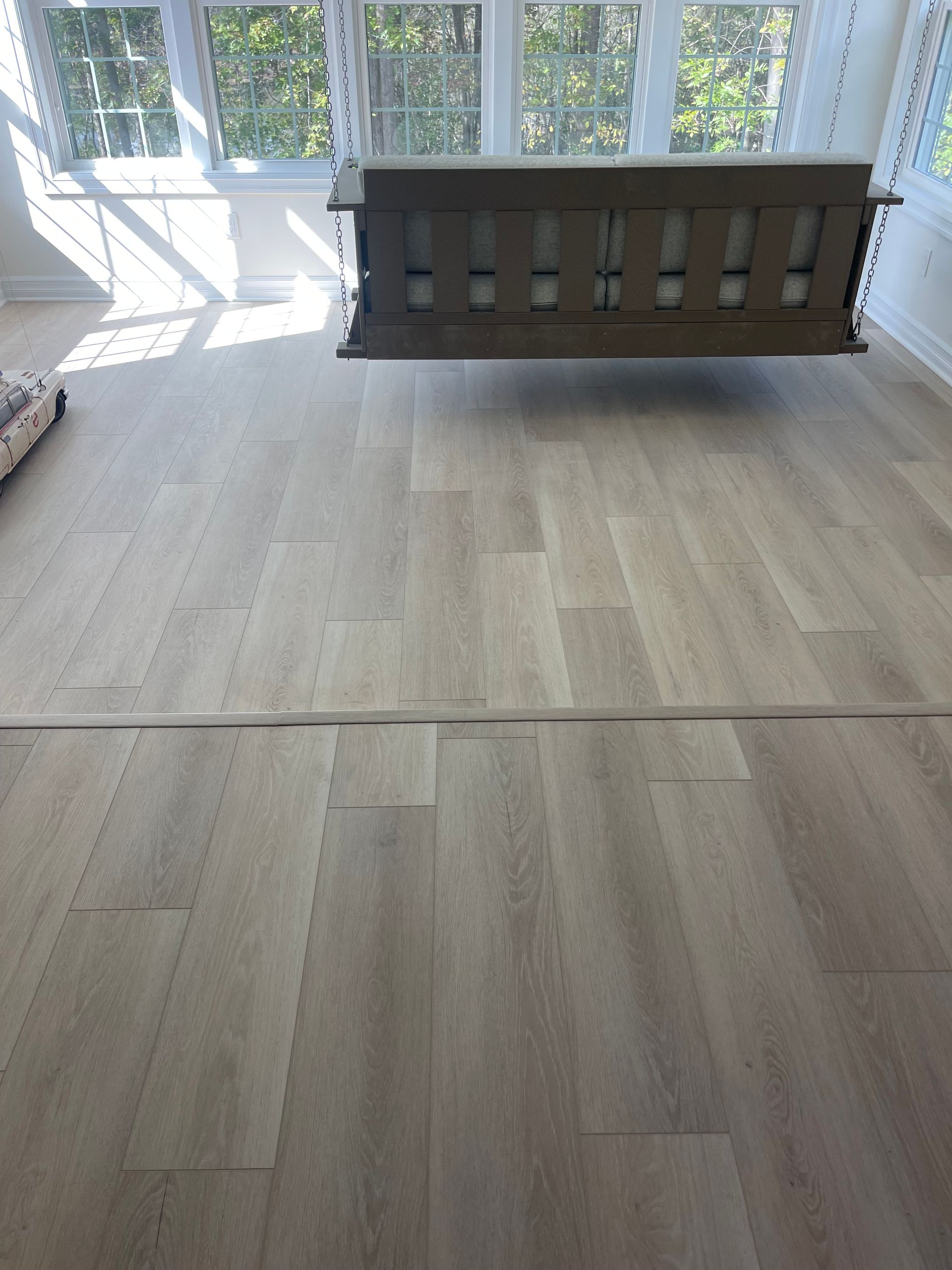 Wooden swing hanging in a light-filled room with wood-look flooring.