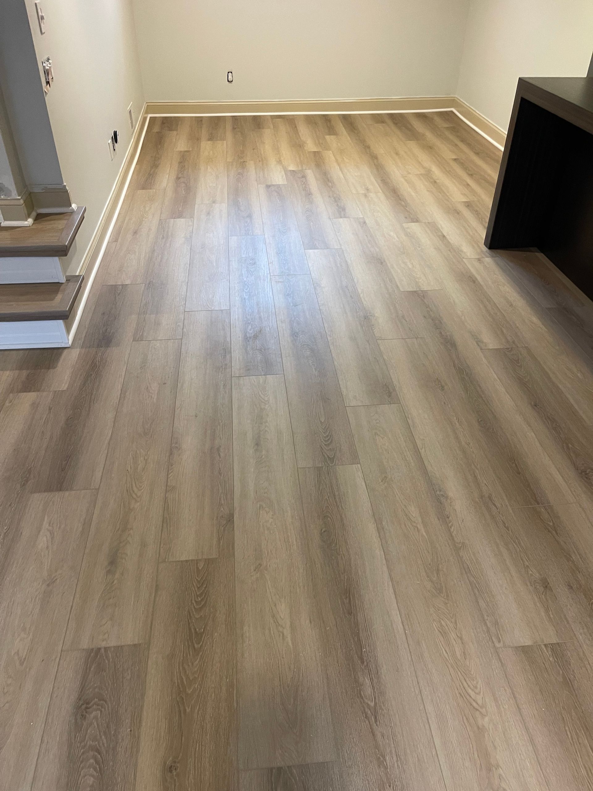 Tan wood-look flooring installed in a room, with white baseboards and a partially visible dark countertop.
