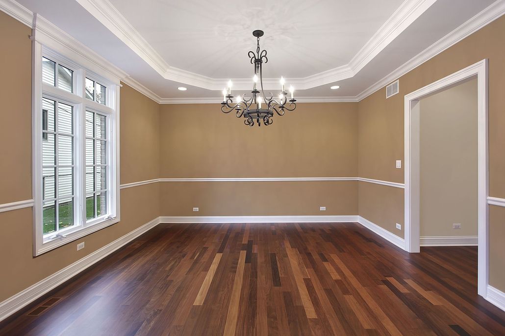 Empty room with brown walls, dark wood floor, white trim, and a chandelier.