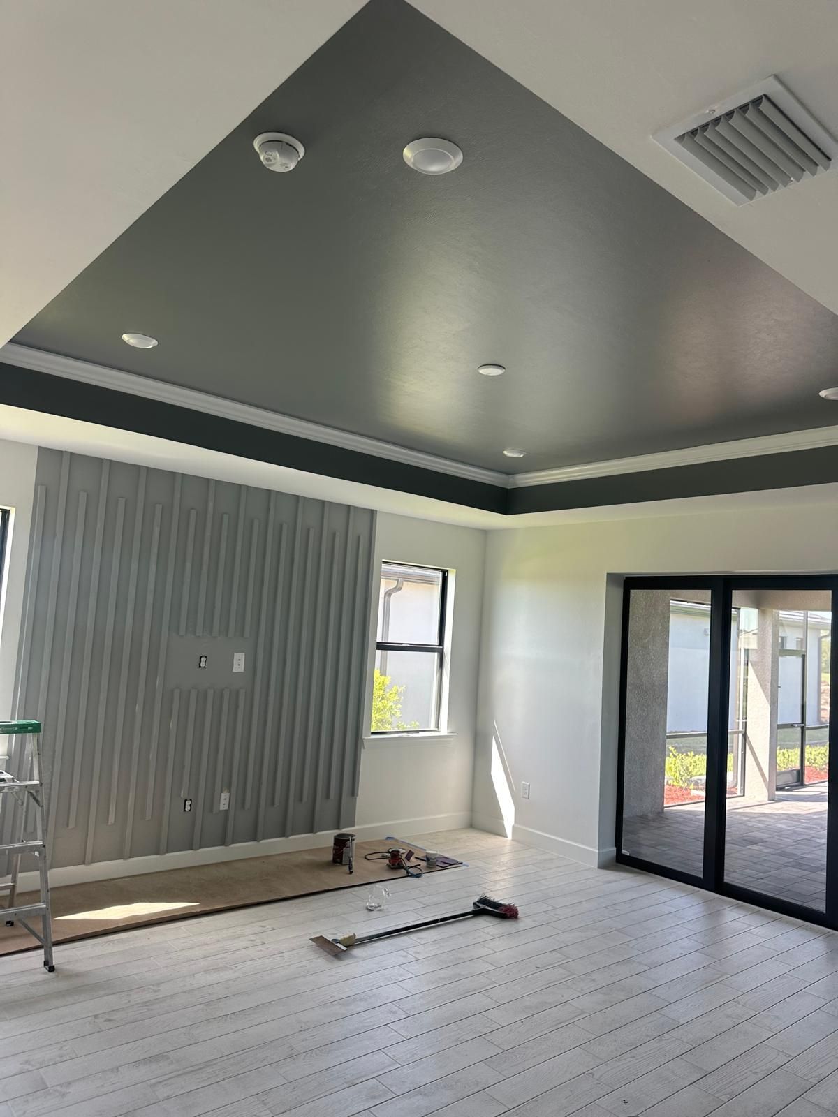Newly renovated room with a grey angular ceiling and white walls, featuring a textured wall panel and sliding glass doors.