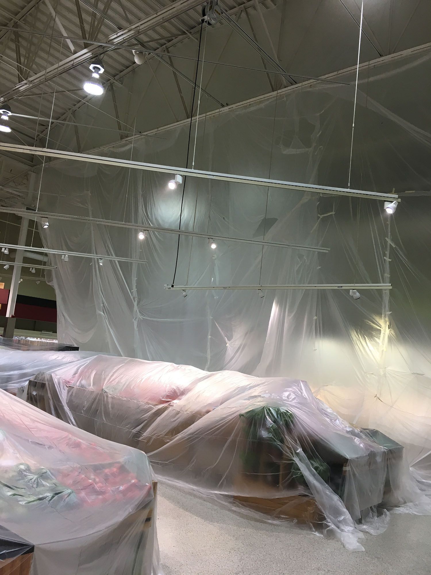 Large room with plastic sheeting creating enclosed spaces, possibly for construction or painting.