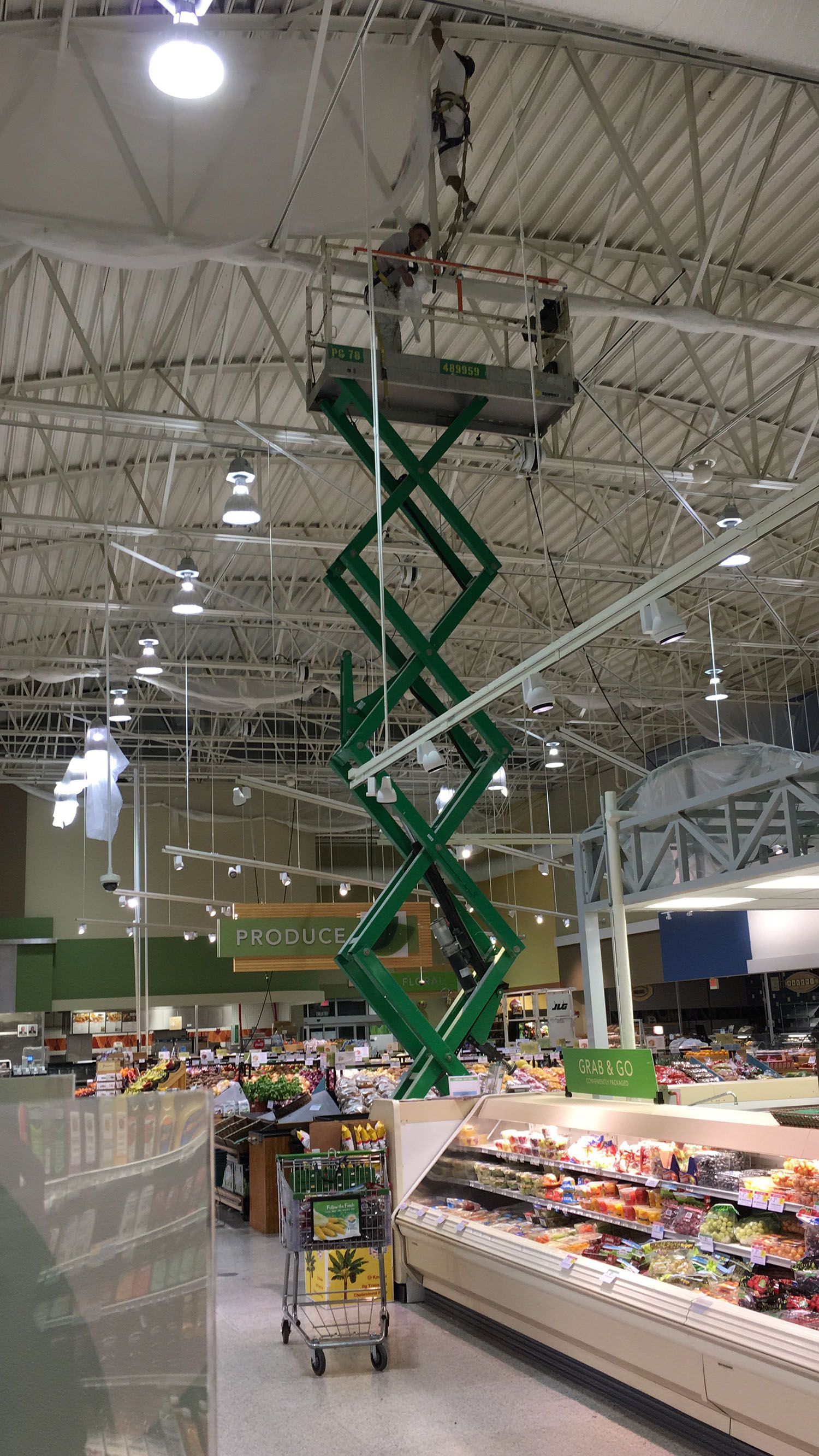 A man is standing on a scissor lift in a grocery store.