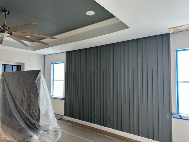 Room with a dark grey accent wall featuring vertical panels, a grey ceiling, and windows with blue tape.