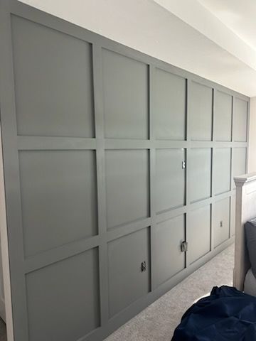 Gray built-in storage unit with paneling and doors. It has rectangular framing and is in a bedroom setting.