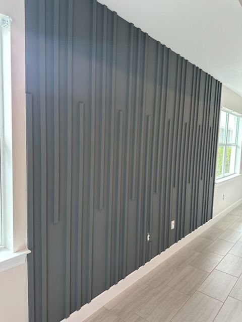 Gray, textured accent wall with vertical grooves, between two windows in a room with light-colored flooring and trim.