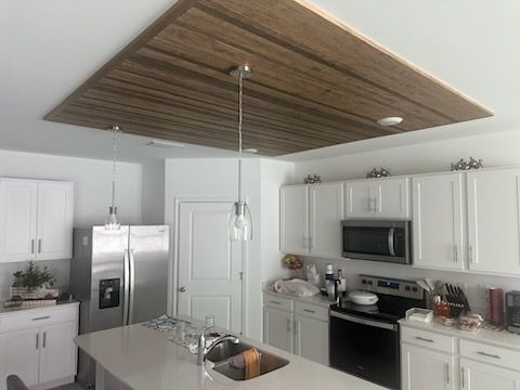 Kitchen with a wooden ceiling accent, white cabinets, stainless steel appliances, and pendant lights.