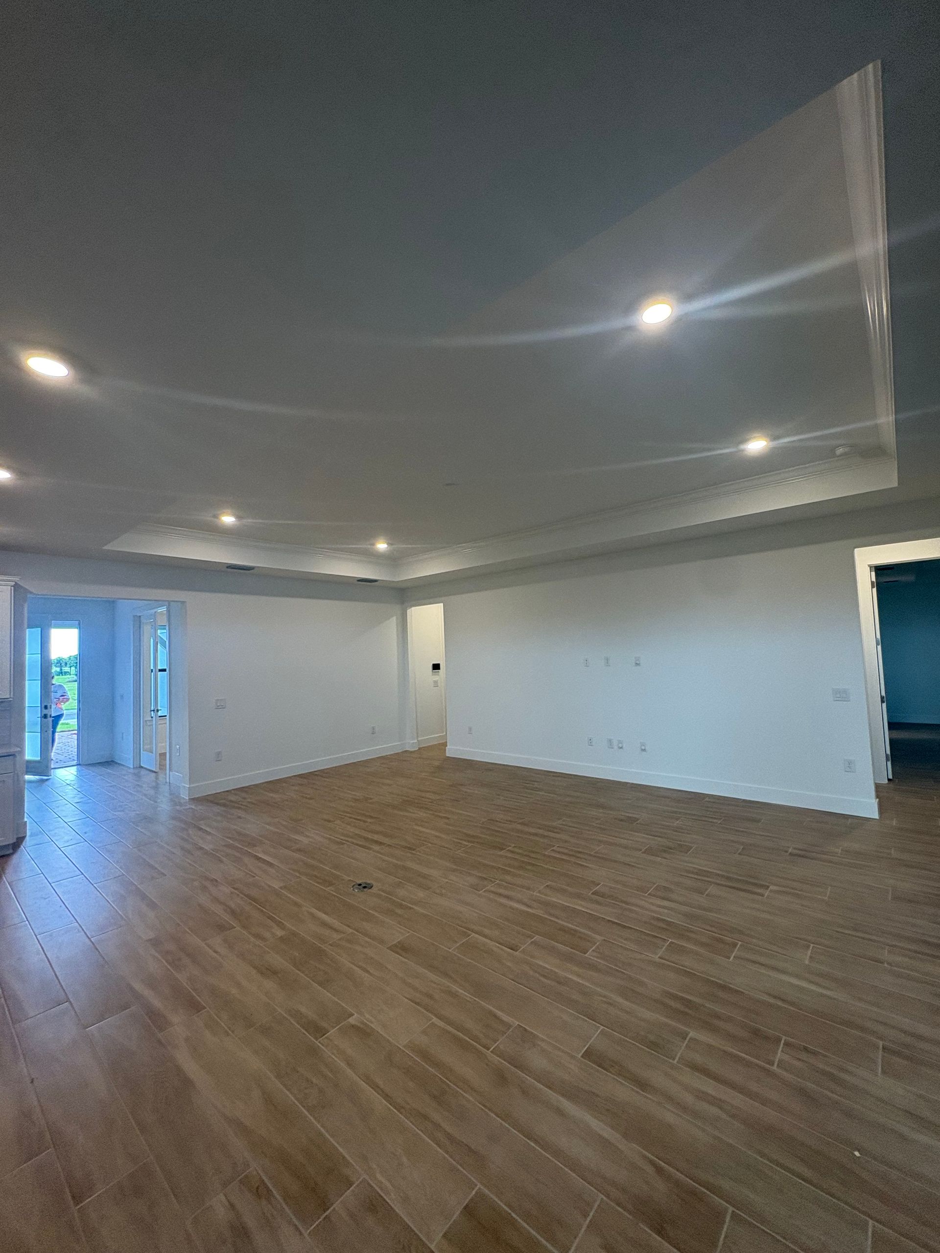 Empty room with wood-look flooring and white walls. Recessed lighting illuminates the space, with an arched ceiling section.