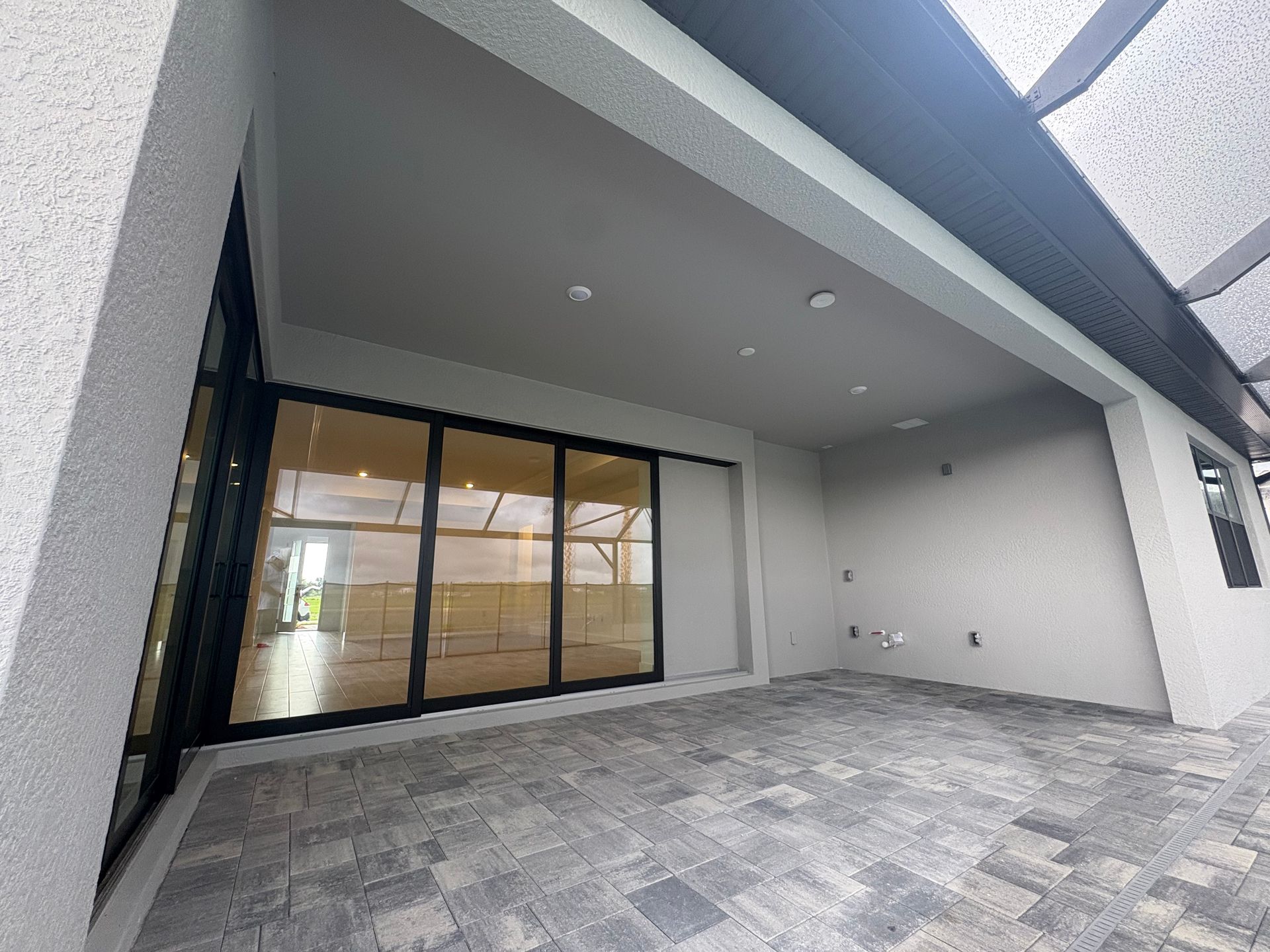 Exterior patio with gray stone flooring, leading to a covered area with a glass sliding door, gray walls, and a modern design.