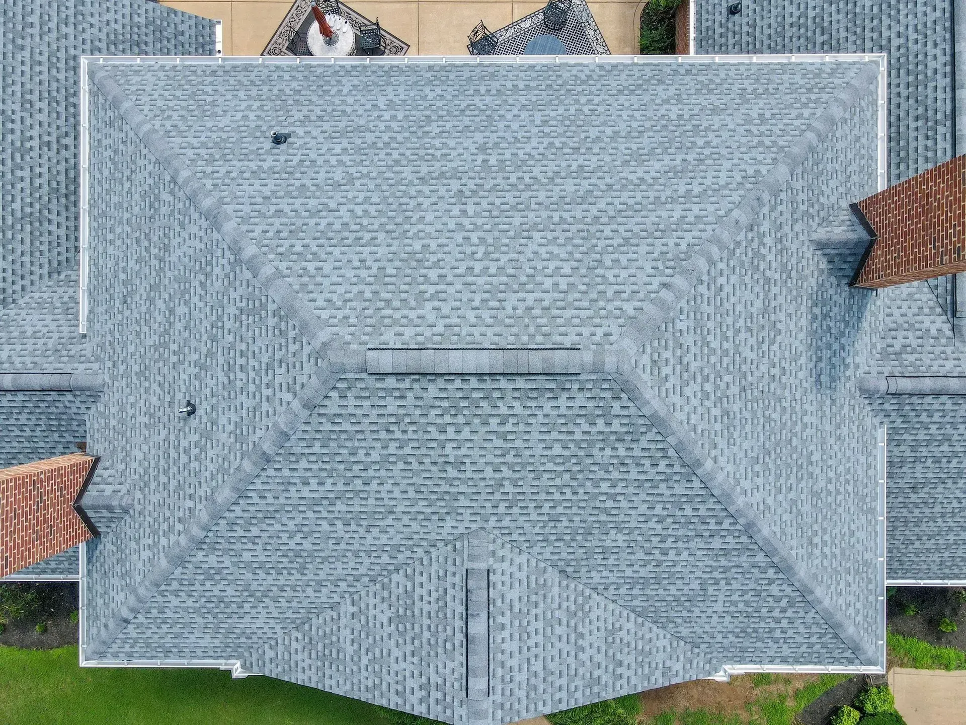 Gray shingled roof with a central vent against a patterned background.