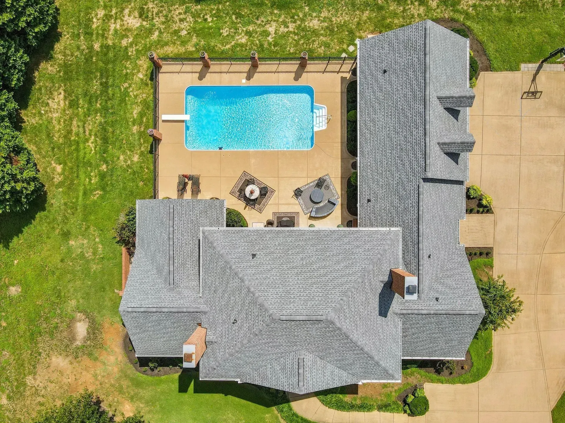 Aerial view of a gray-roofed house with a backyard pool, patio seating, and lawn.