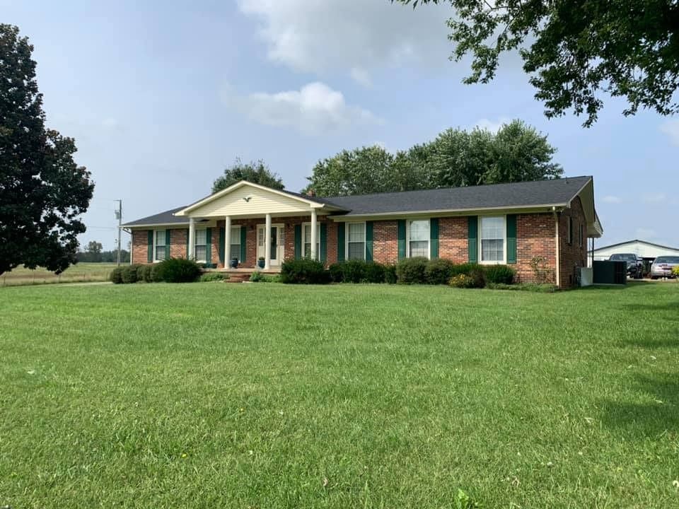 Brick ranch house with white columns and a large green lawn under a partly cloudy sky