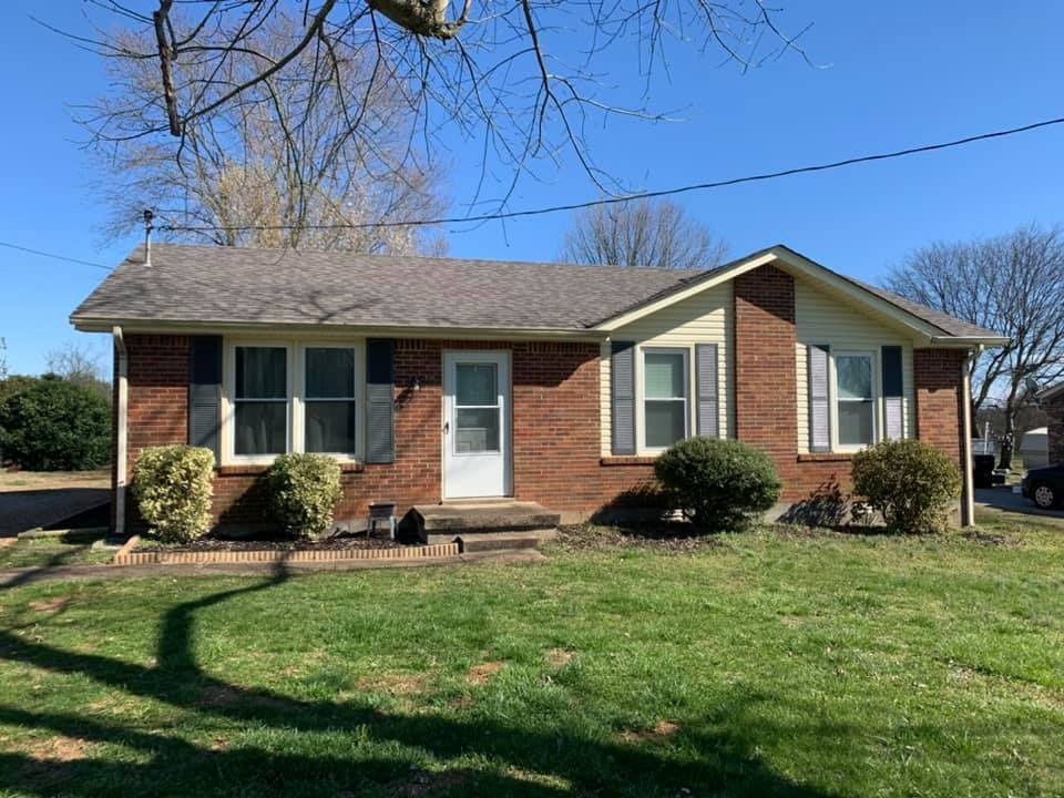 Single-story brick house with white trim, front lawn, and bare trees under a blue sky