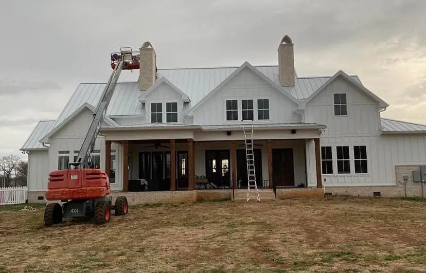 White house under construction with a lift and orange boom lift in the front yard