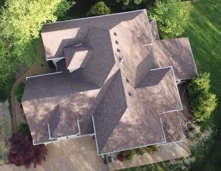 Aerial view of a house with a brown shingled roof surrounded by trees.