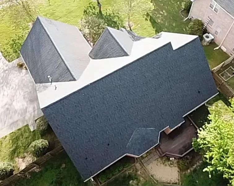 Aerial view of a house with a dark gray roof surrounded by trees and a driveway.