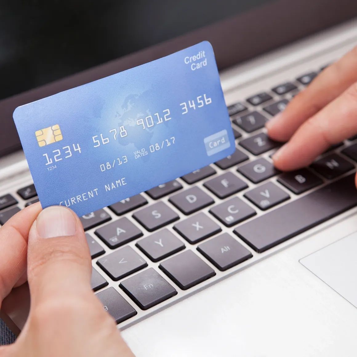 A person holding a credit card over a laptop keyboard