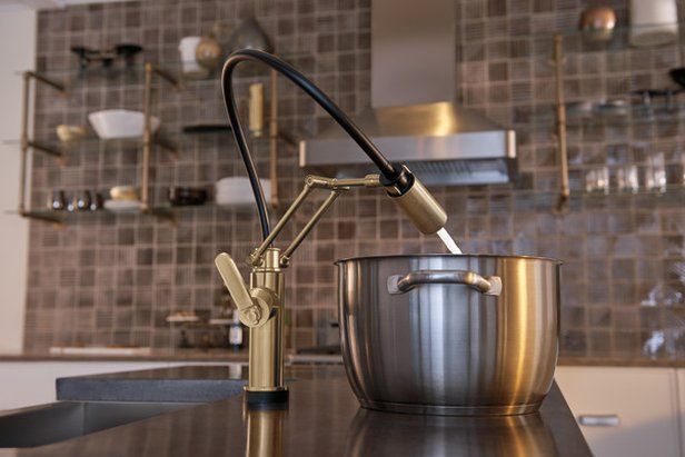 Gold and black kitchen faucet pouring water into a stainless steel pot on a countertop.