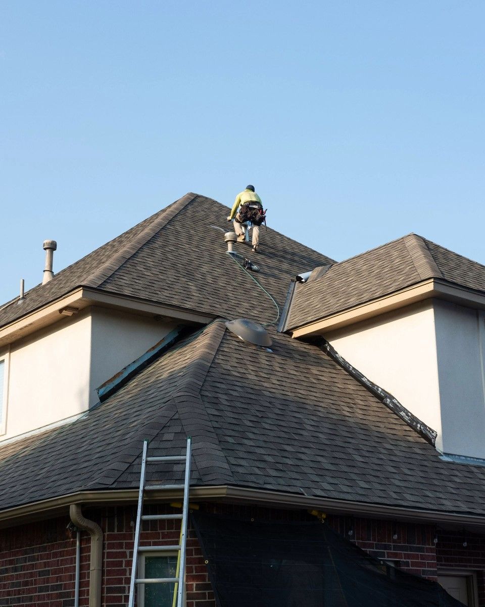 A man is standing on top of a roof next to a ladder.