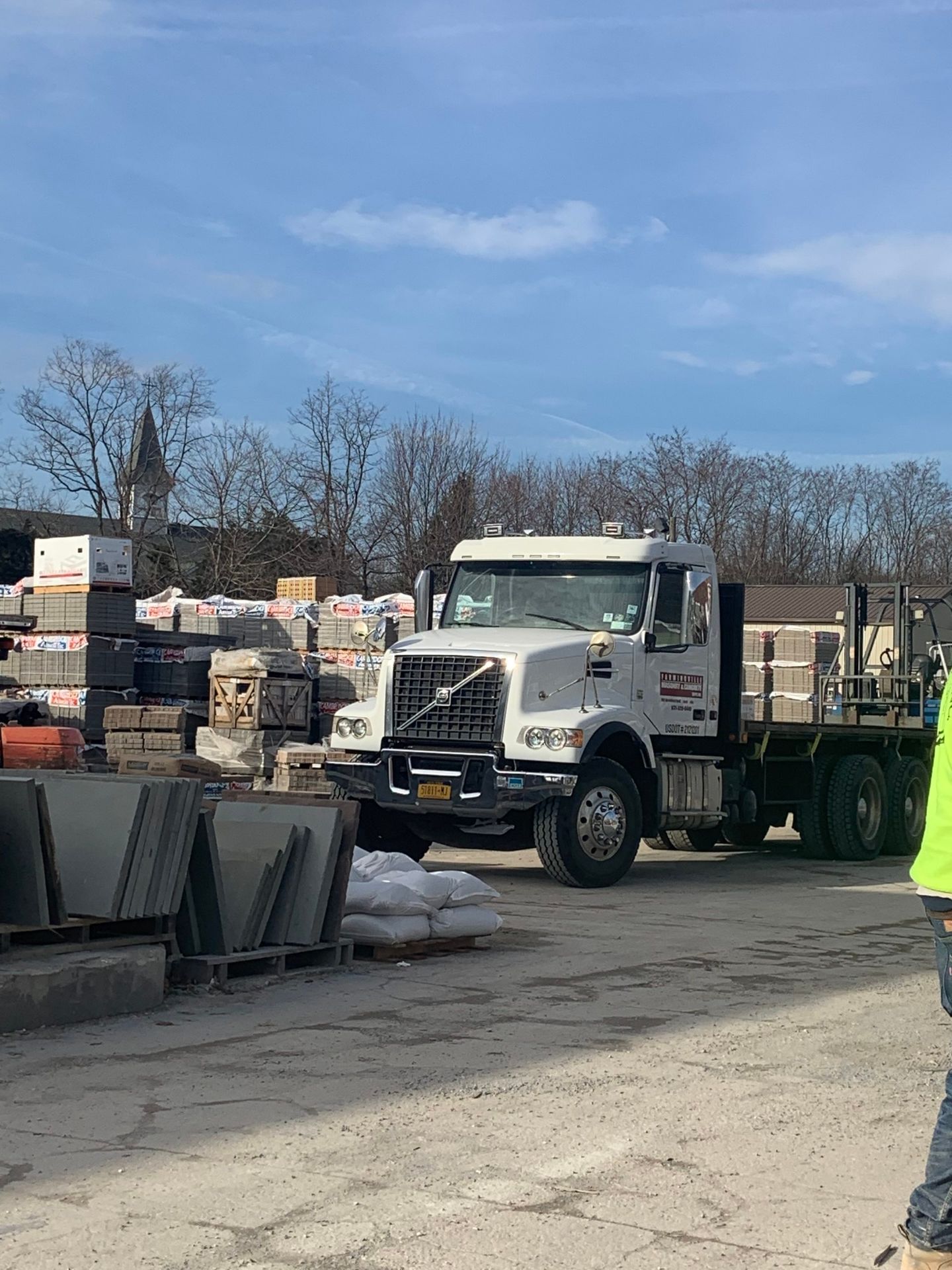 A man in a yellow vest is standing next to a truck in a parking lot