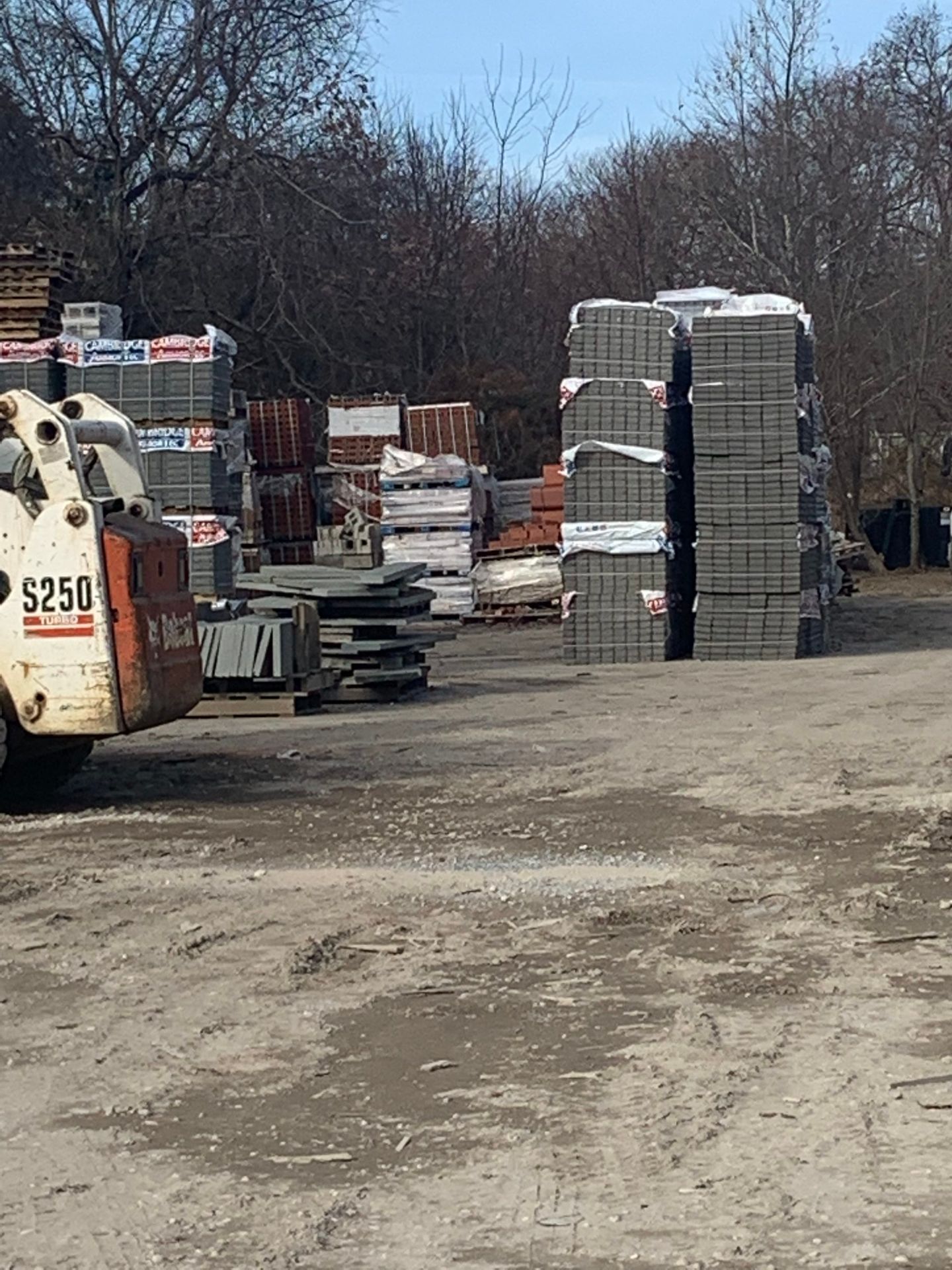 A bobcat truck is parked in a dirt lot next to a stack of bricks.
