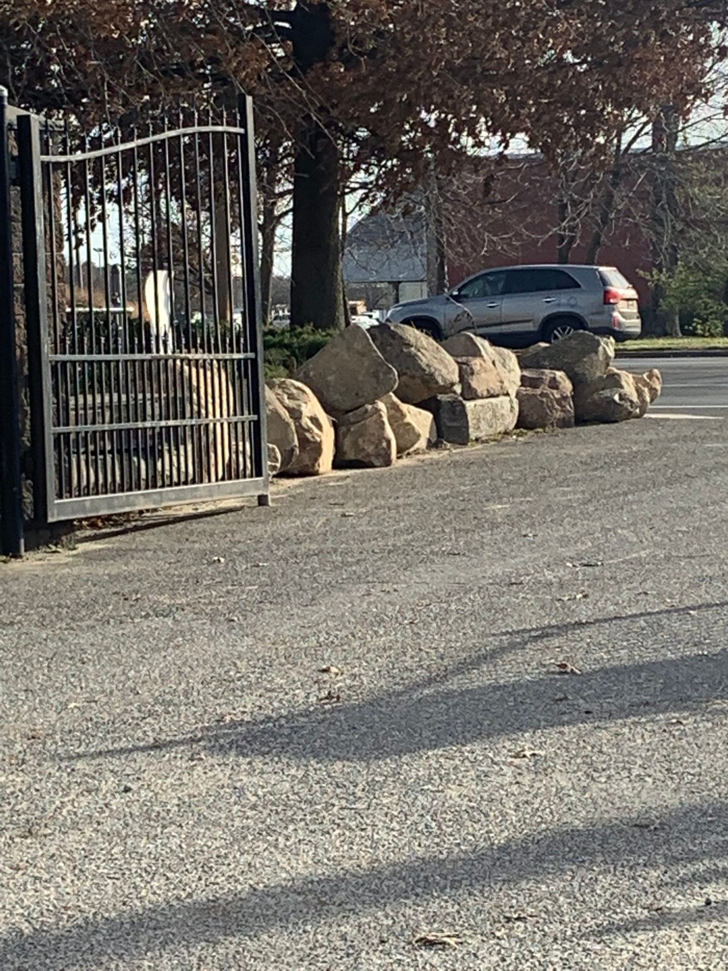 A car is parked in a parking lot next to a fence and rocks.
