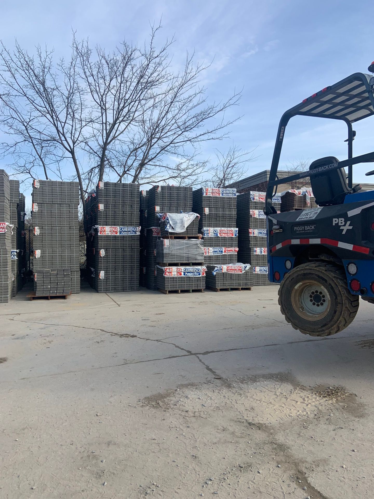 A forklift is driving past a stack of bricks in a parking lot.