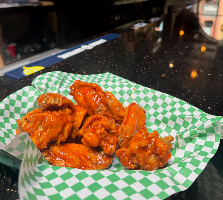 Basket of glazed chicken wings on a bar counter with a green-and-white checkered liner