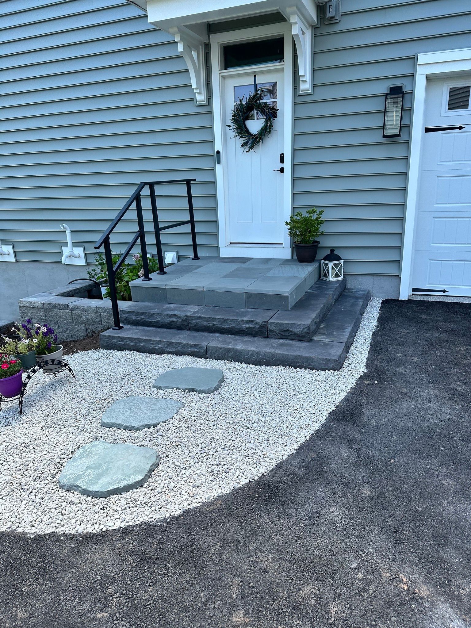 Stone steps lead to a white door with a wreath. Stepping stones path through white gravel.