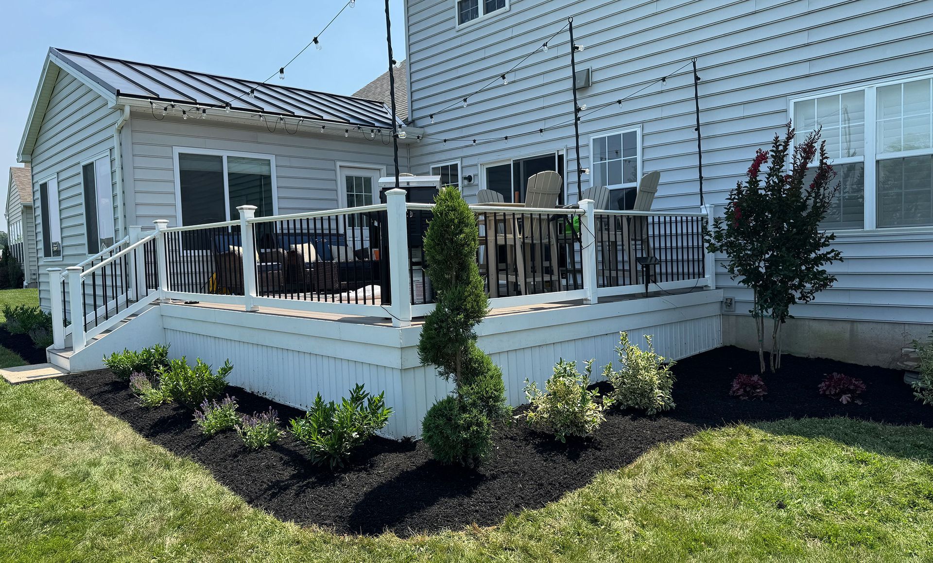 Backyard deck with white railing, black mulch flower bed, and a spiral topiary next to the house.