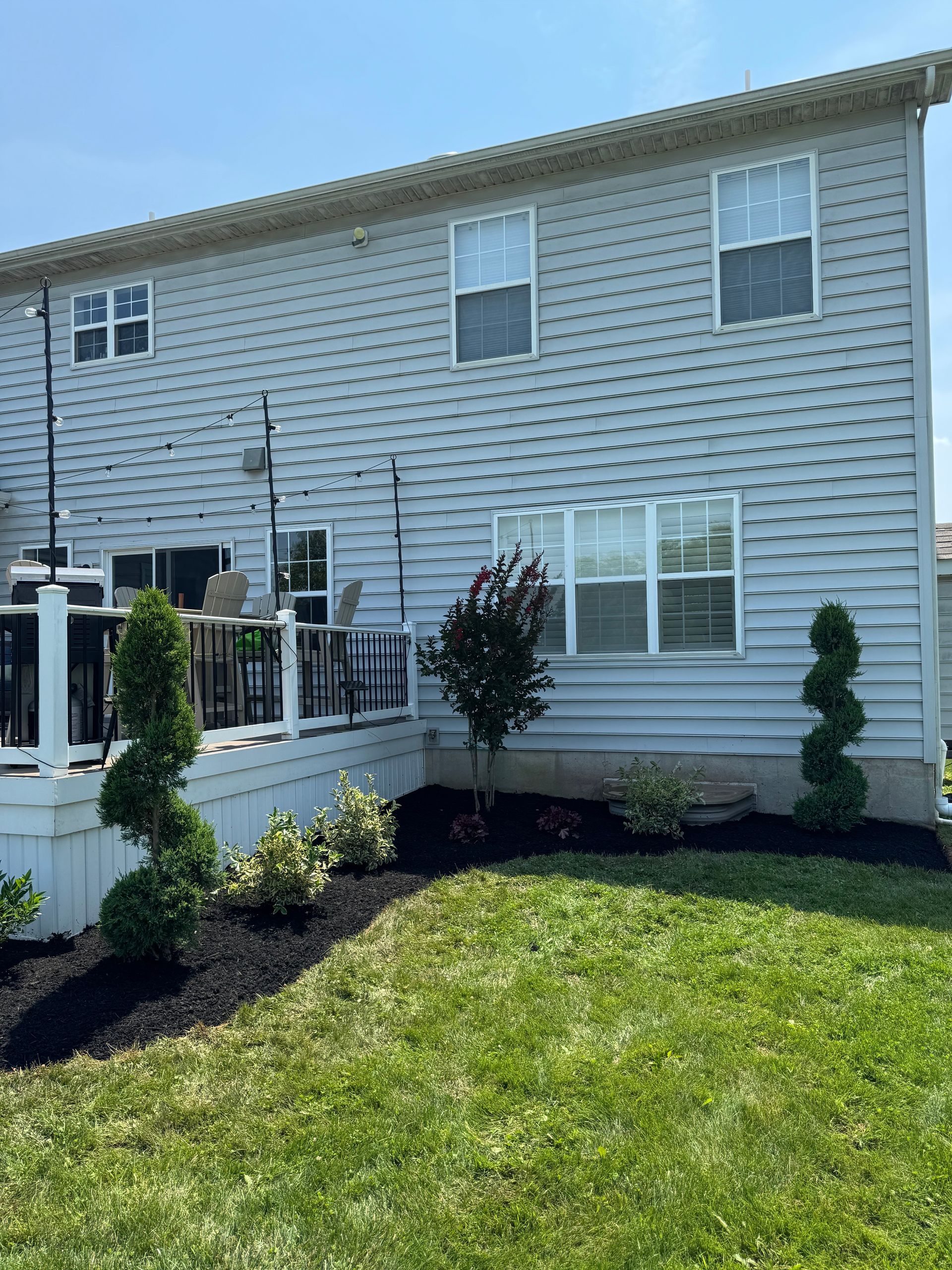 Back of two-story house with light blue siding, deck, and landscaped yard with green lawn.