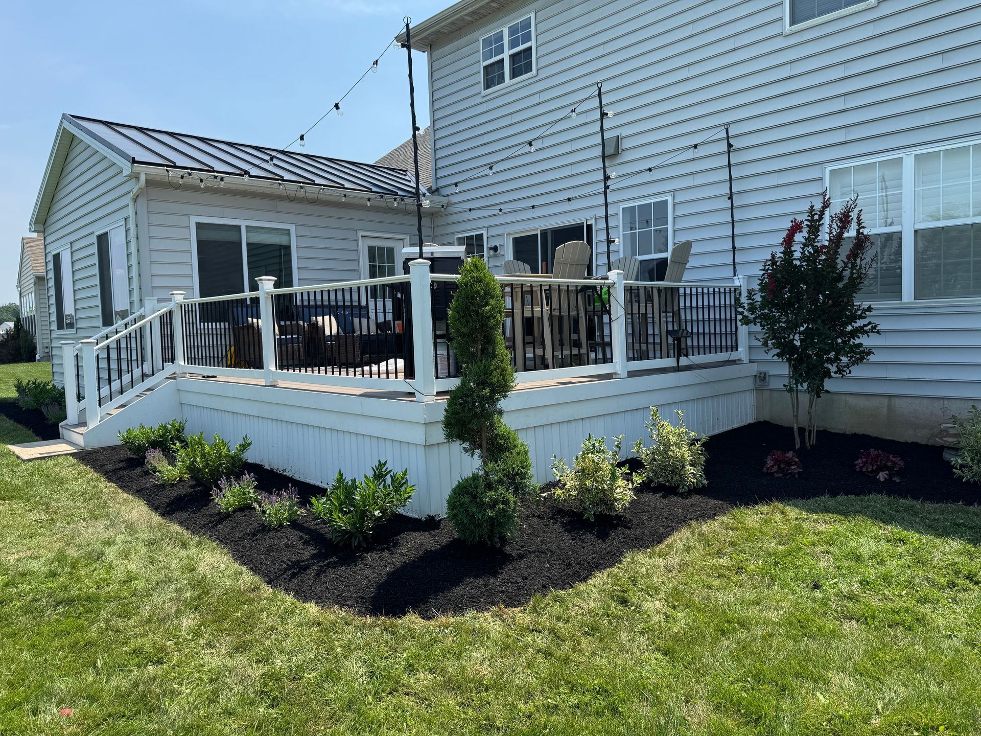 Backyard deck with landscaping, white railing, and string lights; house with gray siding.