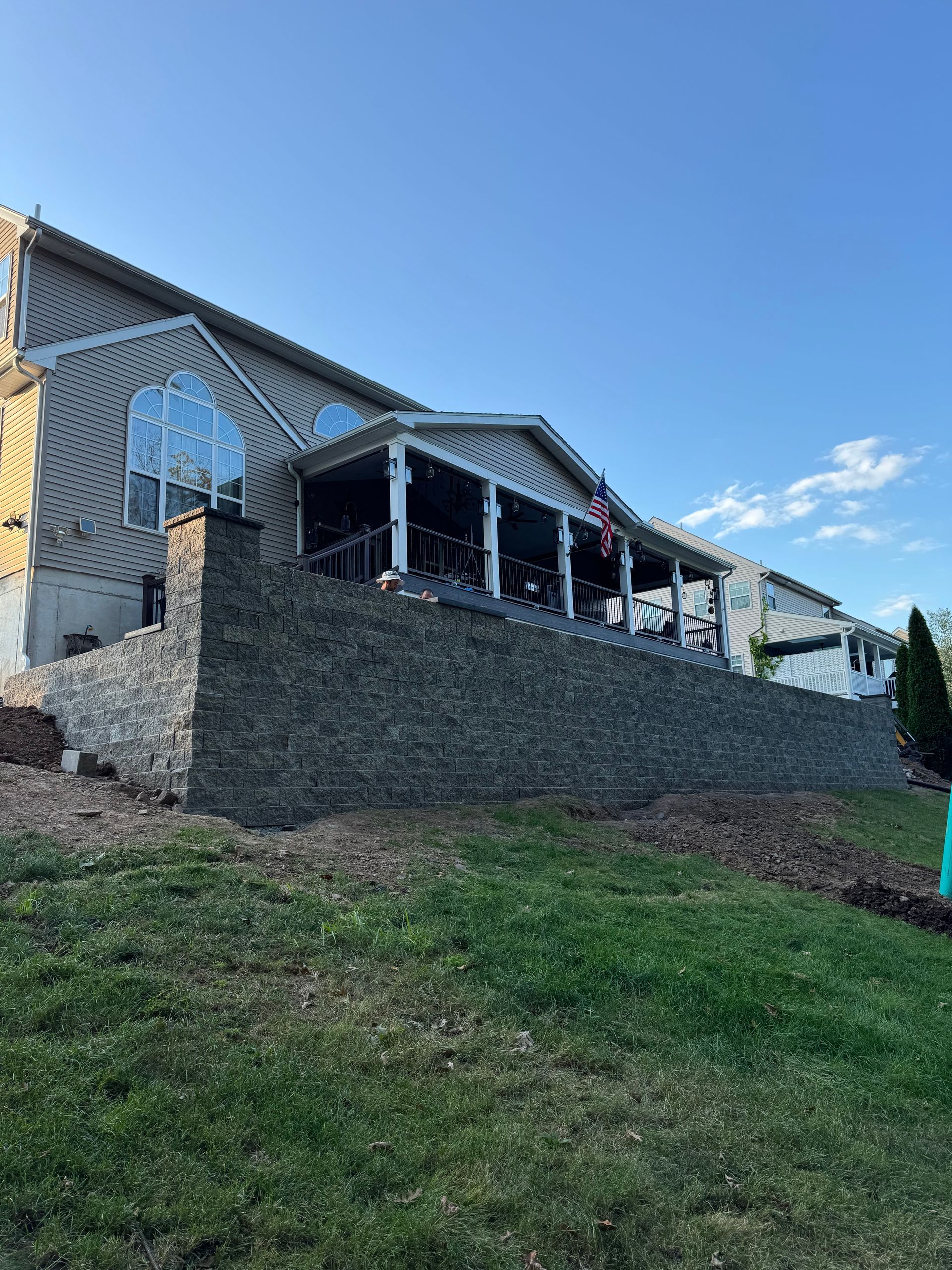 Stone retaining wall supporting a house with a porch and a clear blue sky.