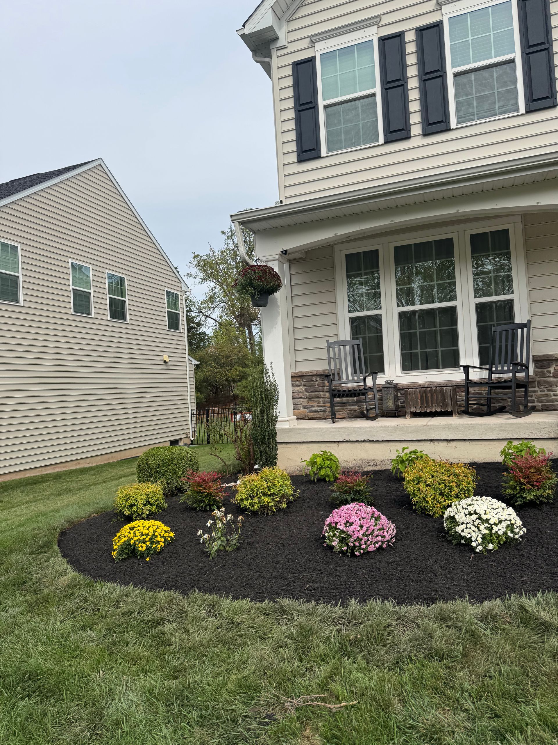 A house exterior with a flowerbed filled with colorful flowers and dark mulch; lawn in foreground.