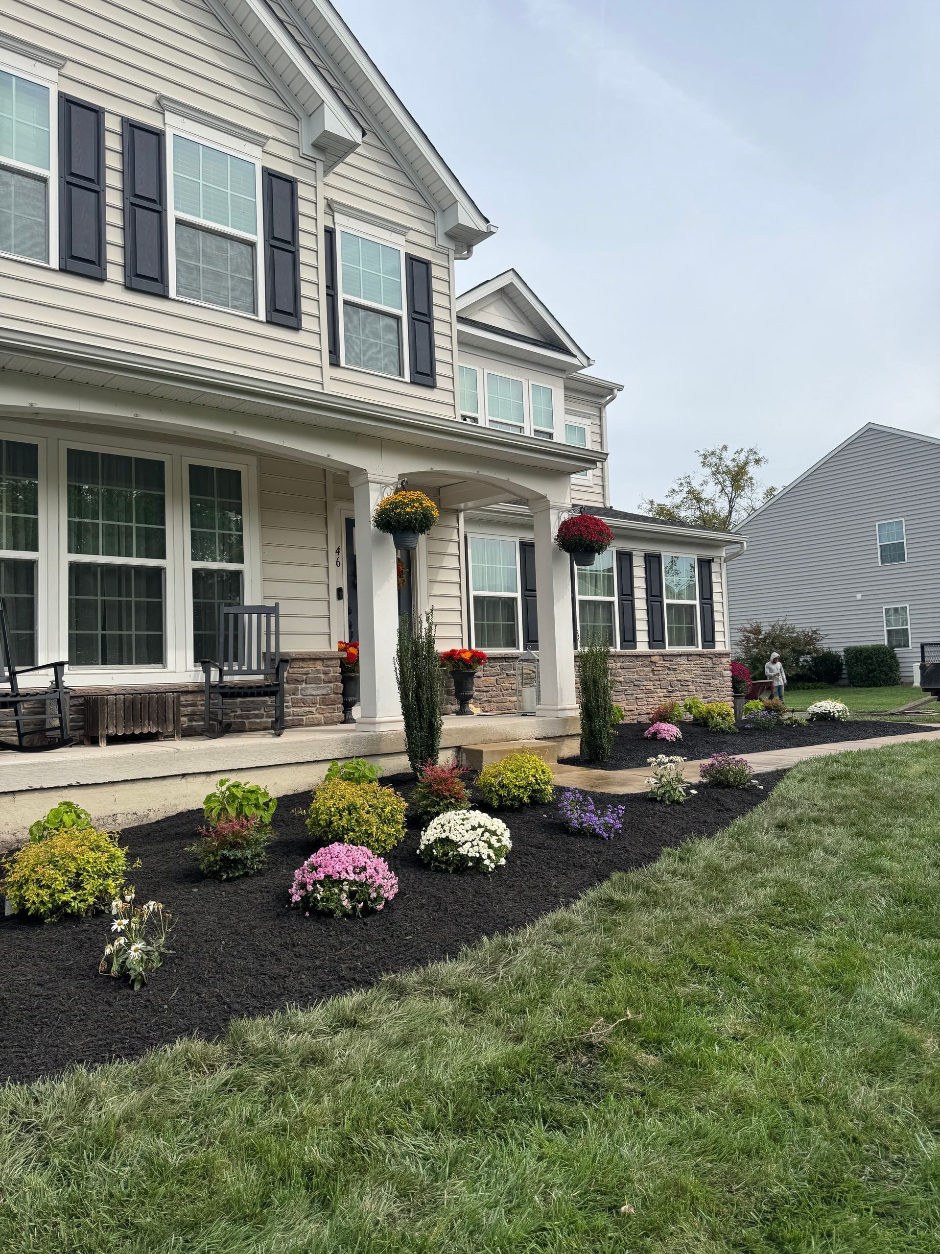 Two-story house with a manicured front yard, black mulch, colorful flowers, and hanging flower baskets.