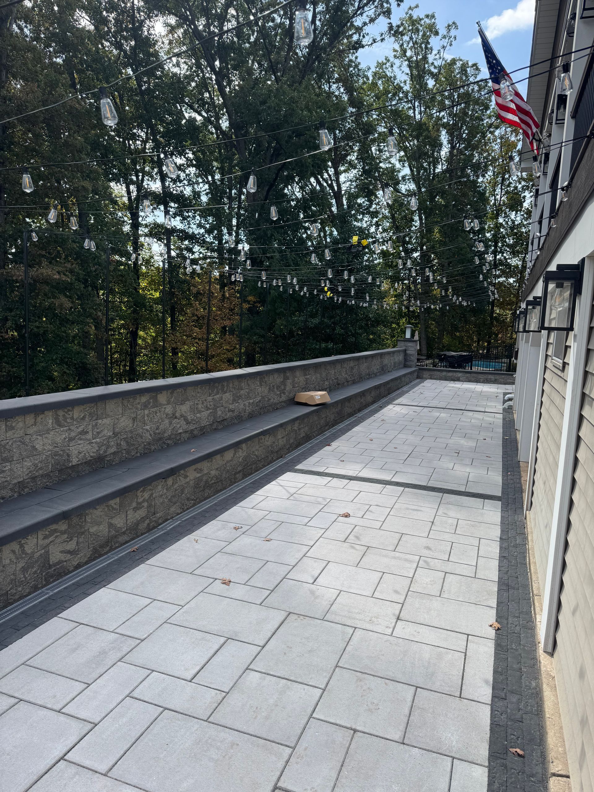 Stone patio with built-in bench, bordered by a wall and a building with an American flag.