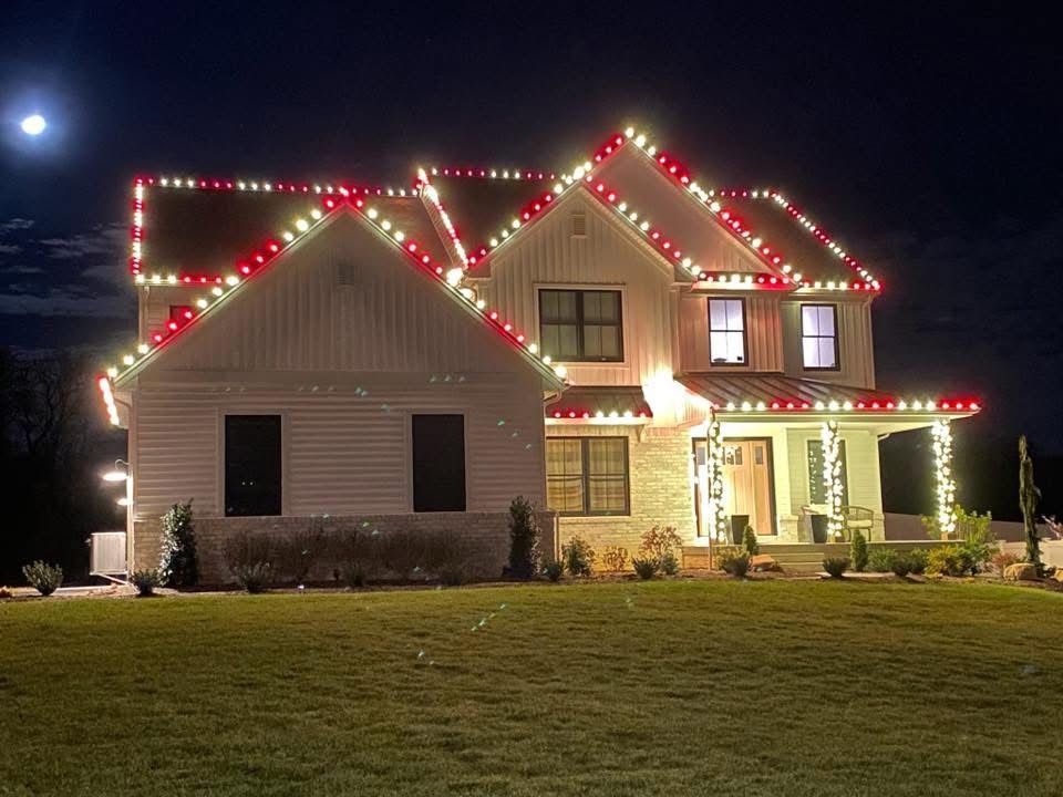 A two-story house at night, decorated with red and white Christmas lights along the rooflines and porch.