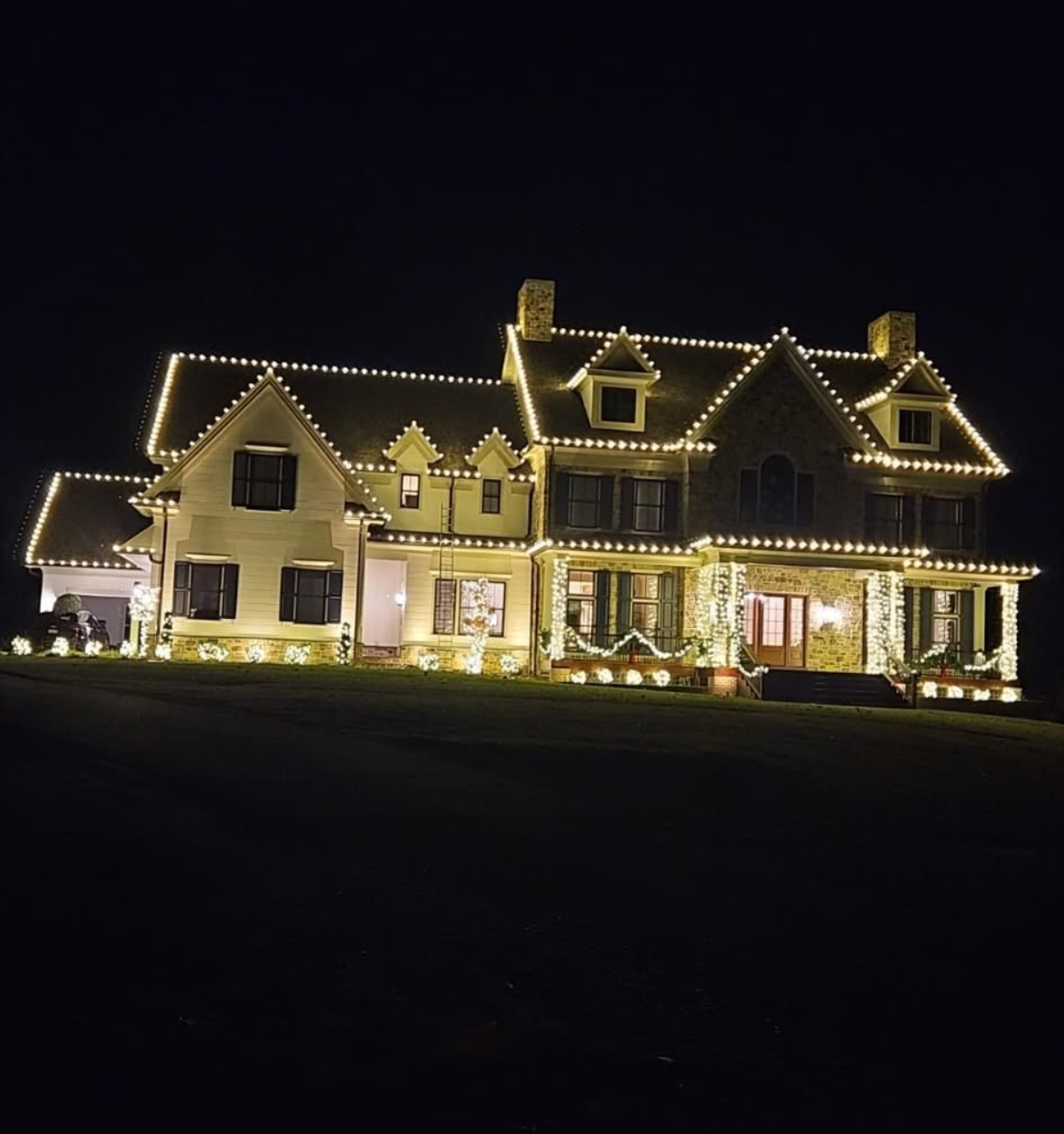Large two-story house at night, illuminated with white Christmas lights along the roof and windows.