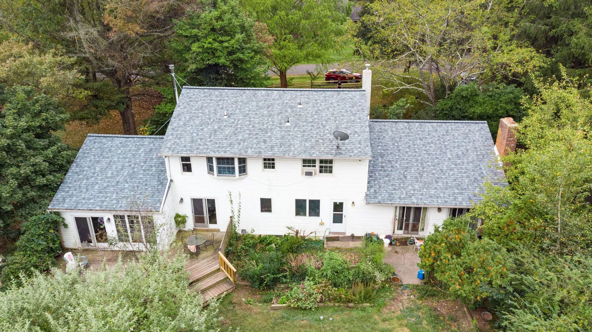 White house with gray roof surrounded by trees and a small garden.