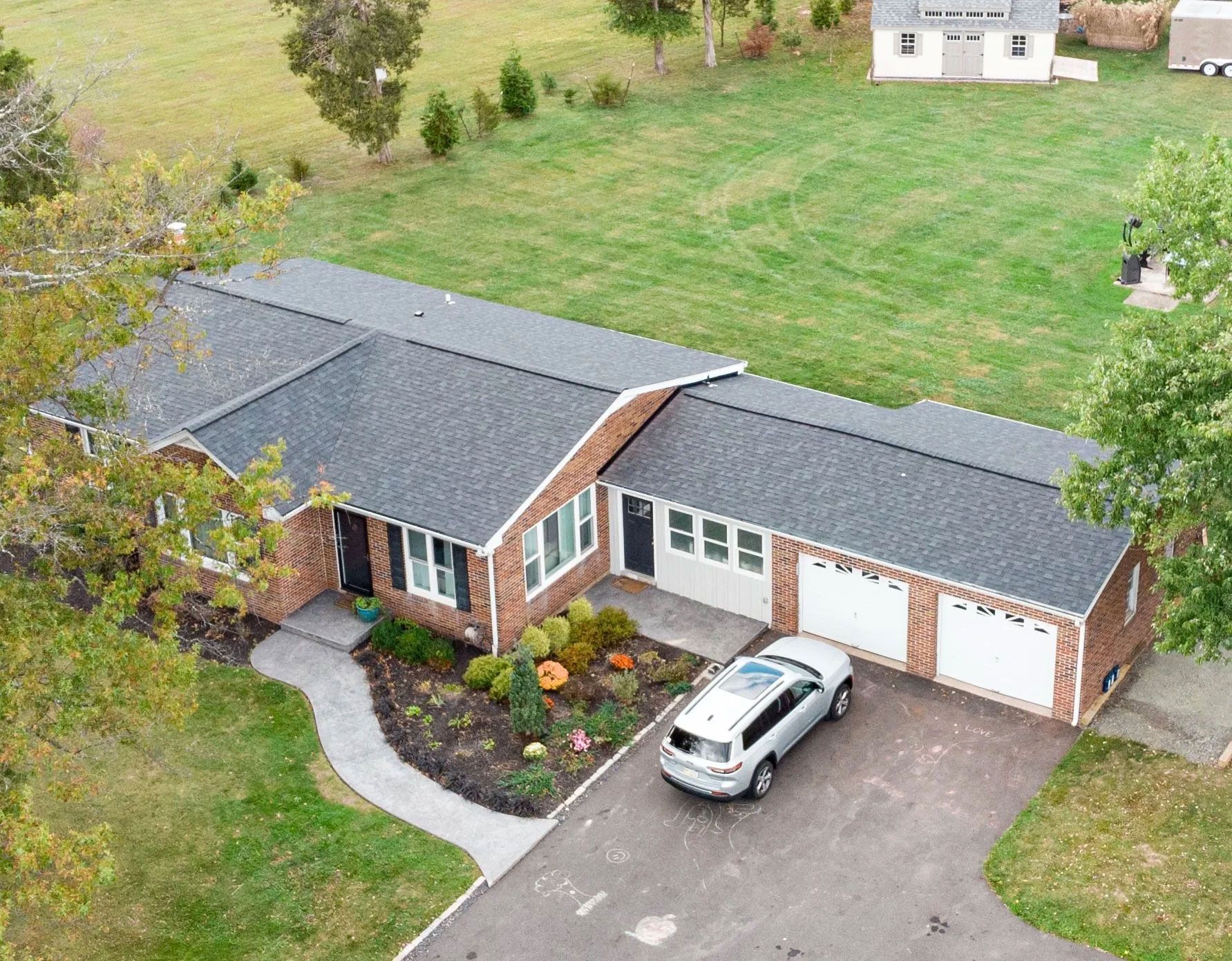 Aerial view of a single-story brick house with a car in the driveway, surrounded by green lawn.