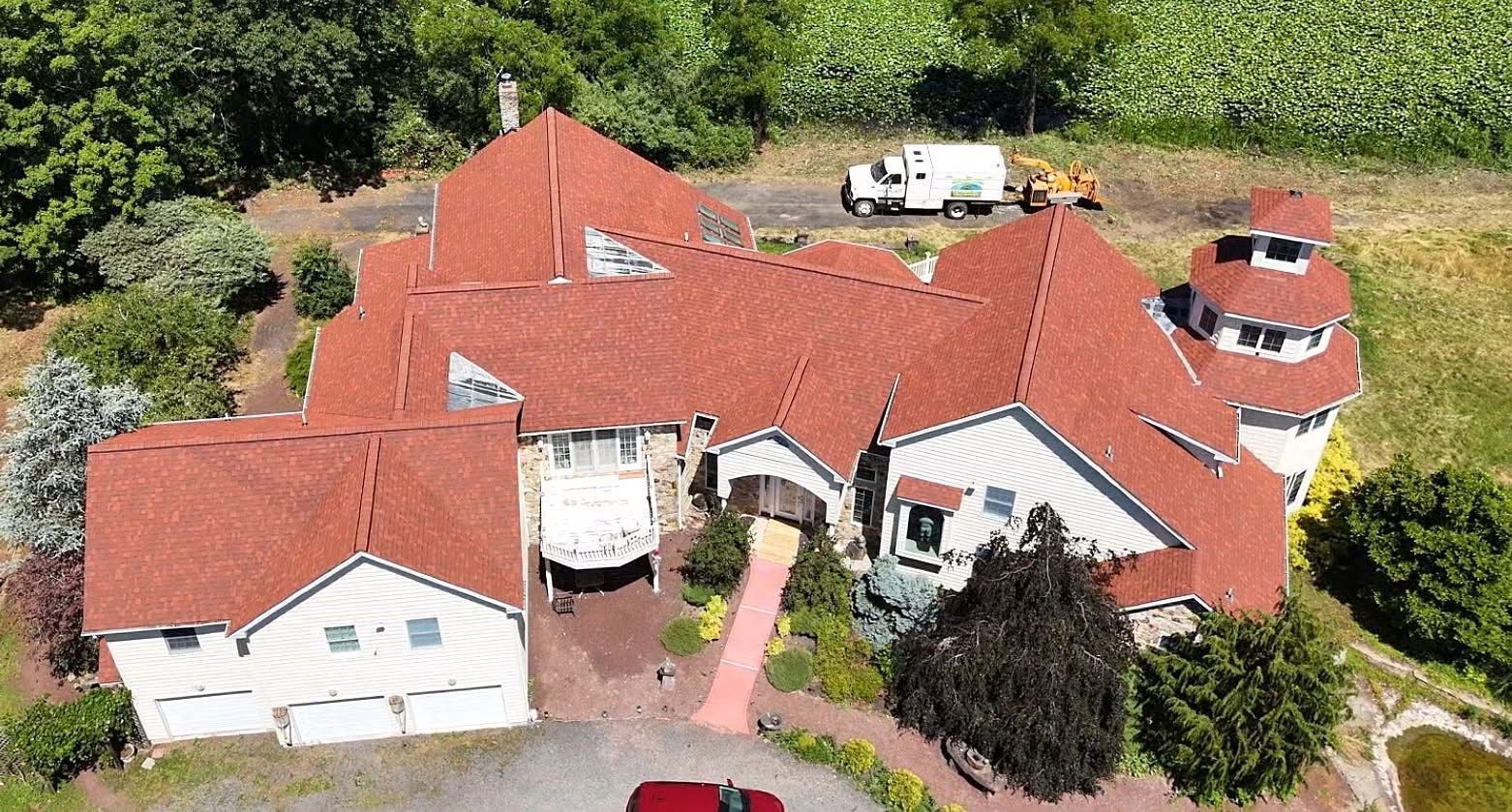Large house with red roof tiles, white siding, and a circular tower, viewed from above.