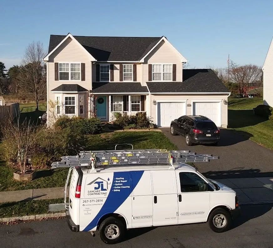 White van with ladder on top parked in front of a two-story house.
