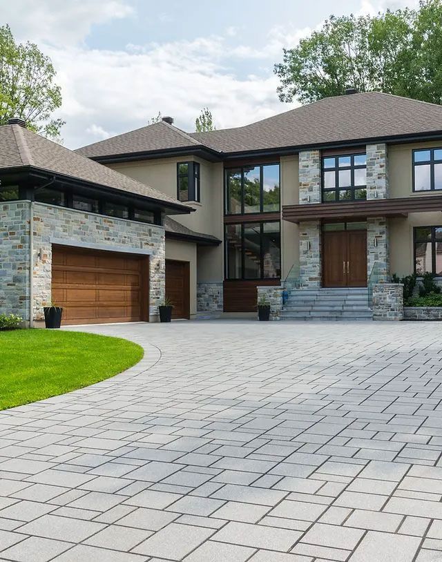 Elegant modern house with a stone and stucco facade, a paved driveway, and a two-car garage.