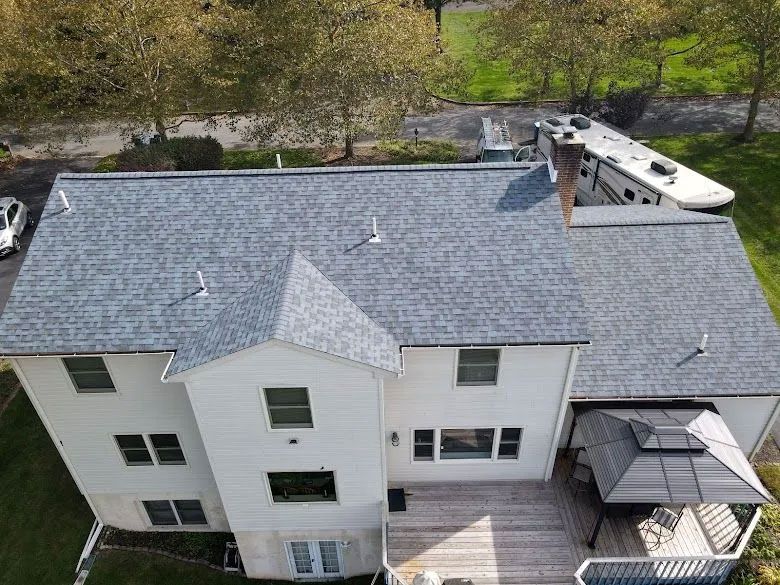 Overhead view of a two-story white house with a gray shingle roof, deck, and RV in the background.